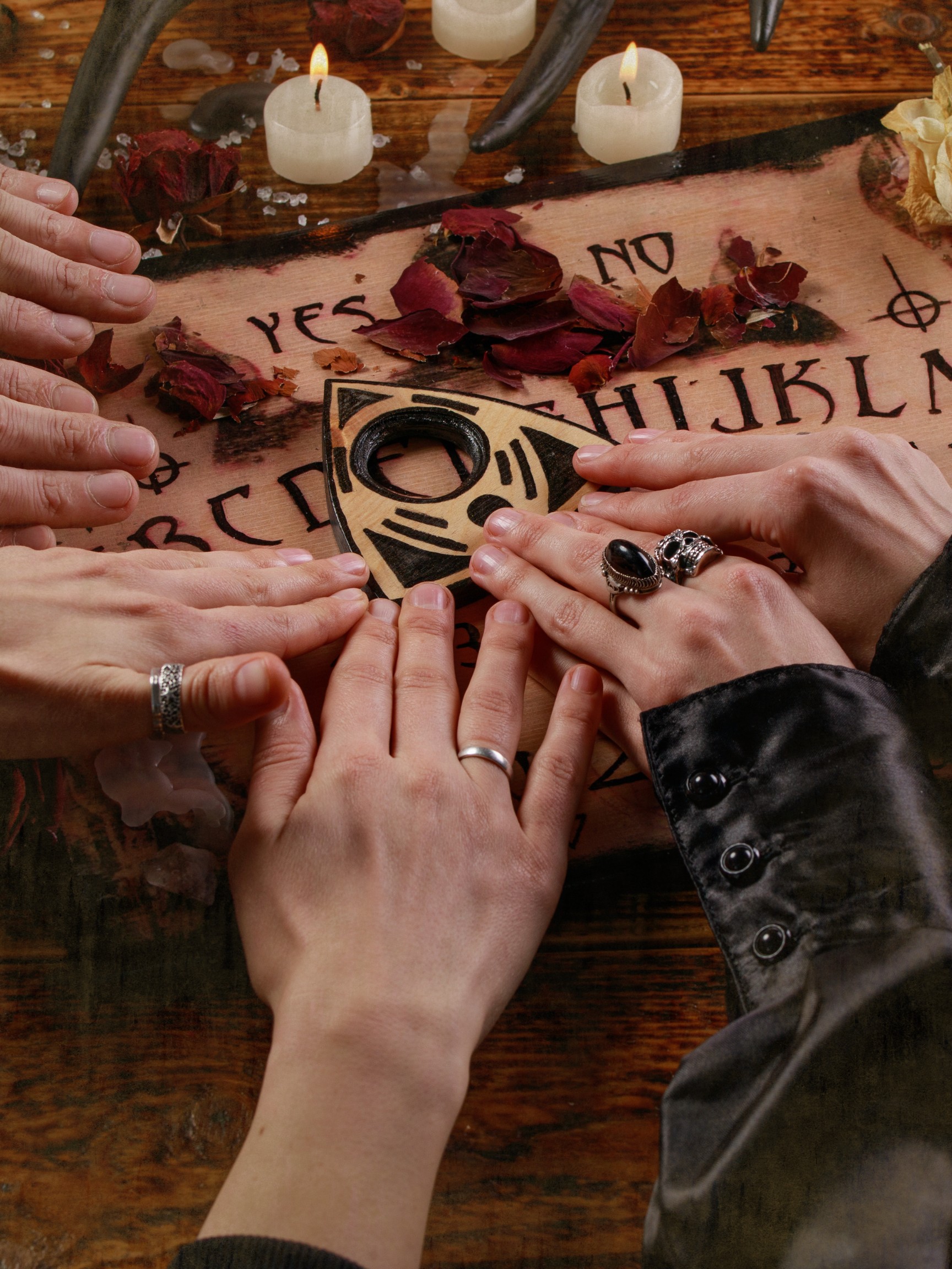 An escape room theme image. Hands on a Ouija board similar to the escape rooms.